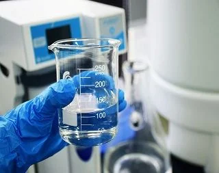 Gloved hand holding a beaker of blue solution in the lab